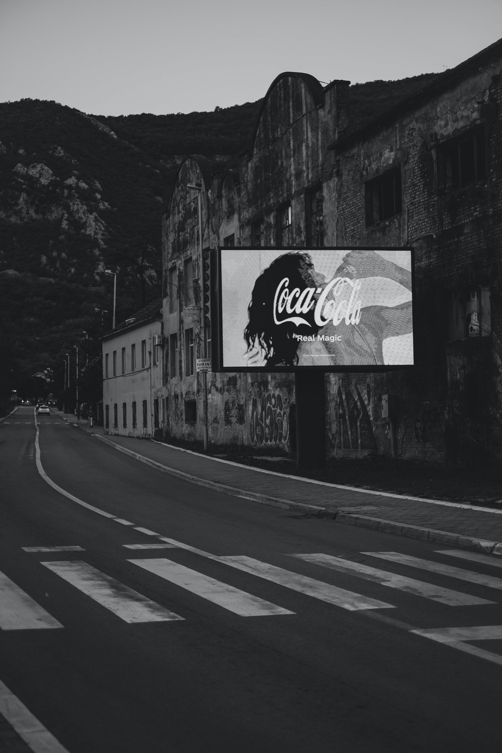 black and white photo of a billboard with a coca cola advertisement with a lady drinking the from the coca cola bottle.